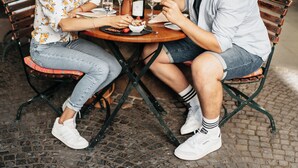 Dos personas cenando en una mesa al aire libre con un pilar de piedra y plantas en macetas.