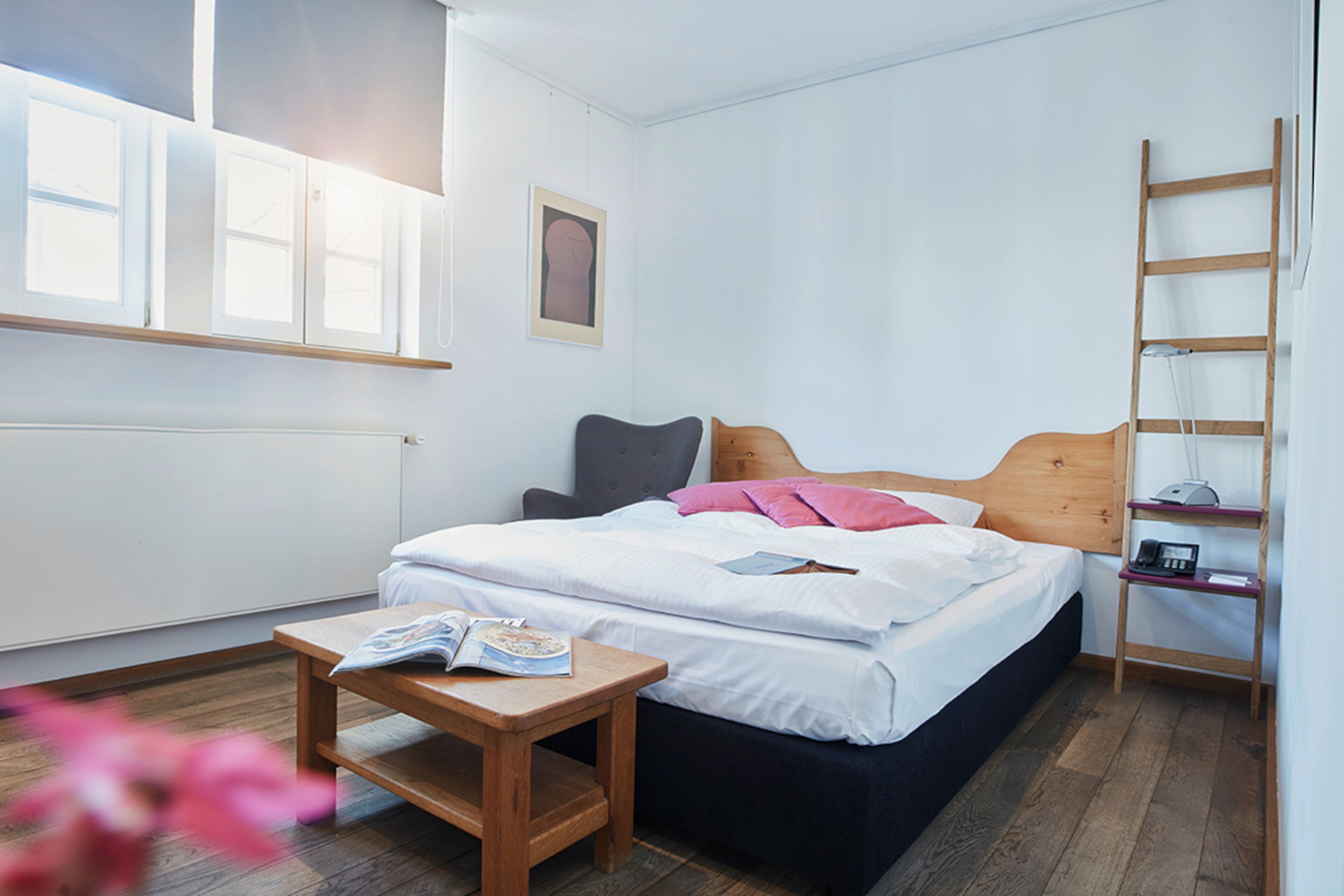 Un dormitorio con cama, mesita de noche y una escalera de madera adosada a la pared.