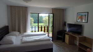 A hotel room with a bed, a desk with a TV, and a balcony with a view of greenery. - Apparthotel Alte Innbruecke (Neuhaus am Inn)