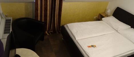 A hotel room with a bed, a chair, a small table, and a curtain.