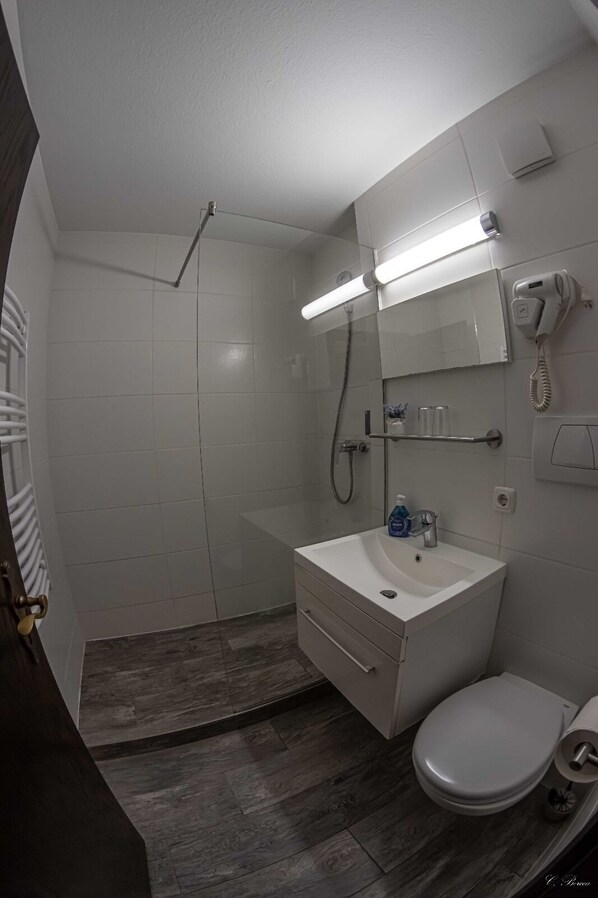 A modern bathroom with a shower, a sink, a toilet, and a hairdryer mounted on the wall.