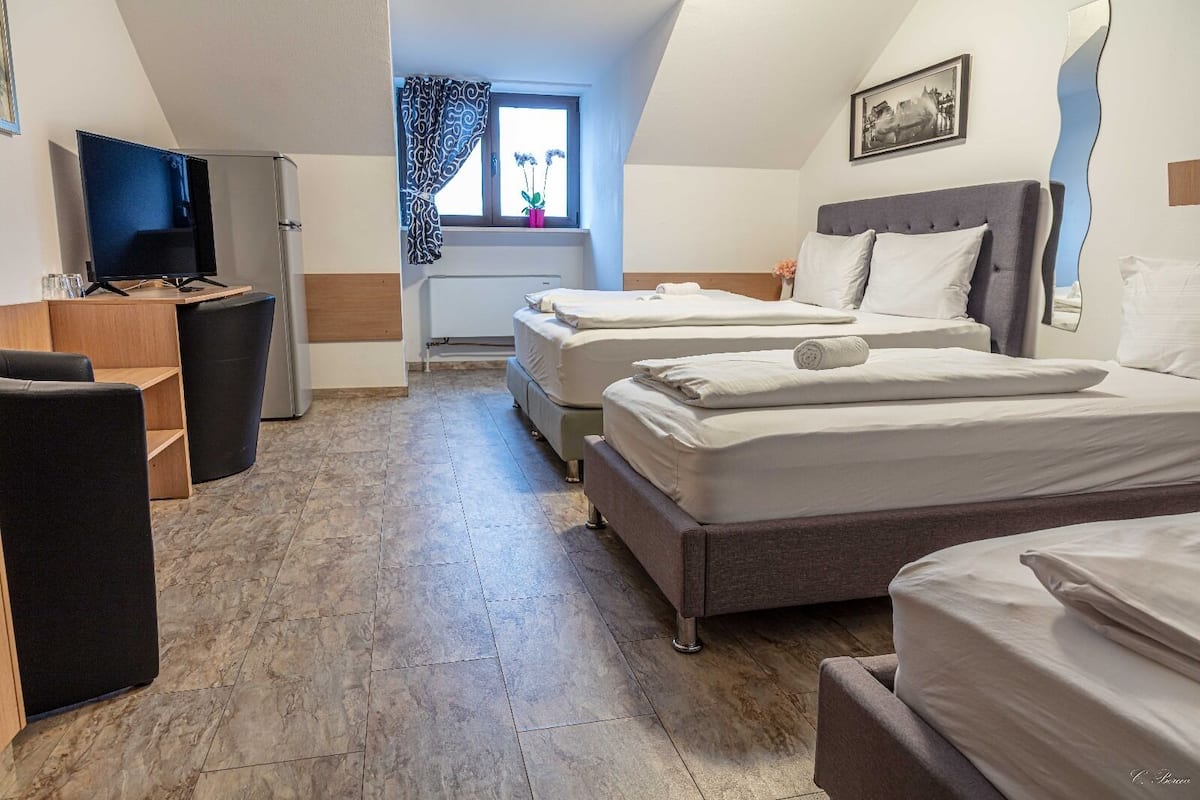 A hotel room with two beds, a TV, a desk, and a window with curtains.