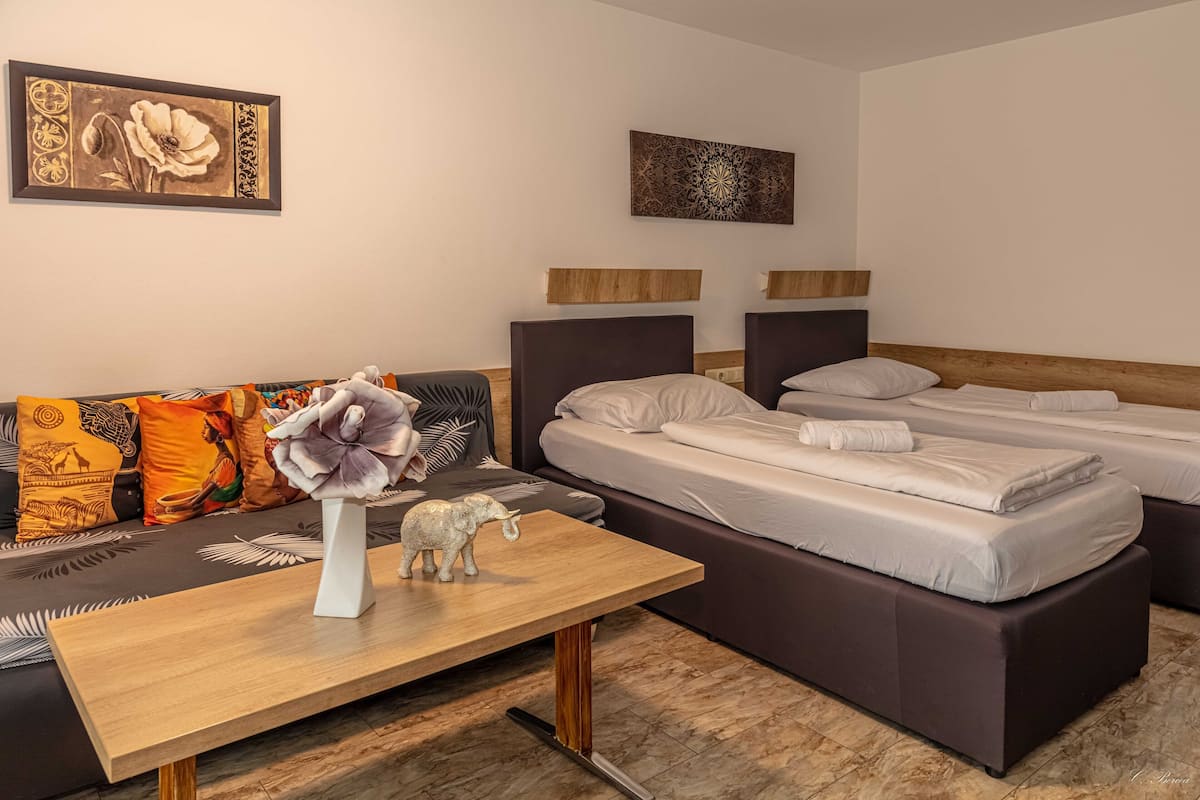 A hotel room with a sofa, two beds, a wooden table, and decorative items.