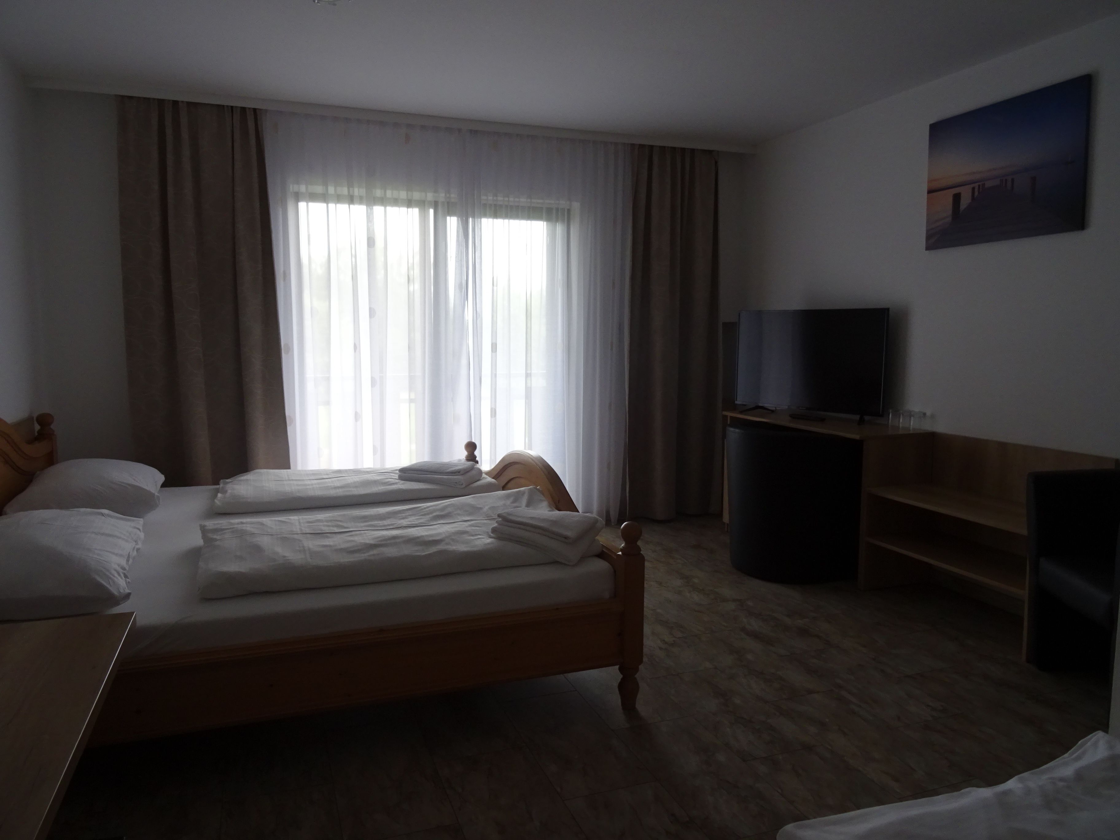Une chambre d’hôtel avec deux lits simples, une télévision, un bureau et une grande fenêtre avec des rideaux.