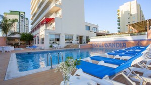 Zona de piscina de hotel con sillones de descanso, piscina y un cartel que dice "HOTEL GANDIA".