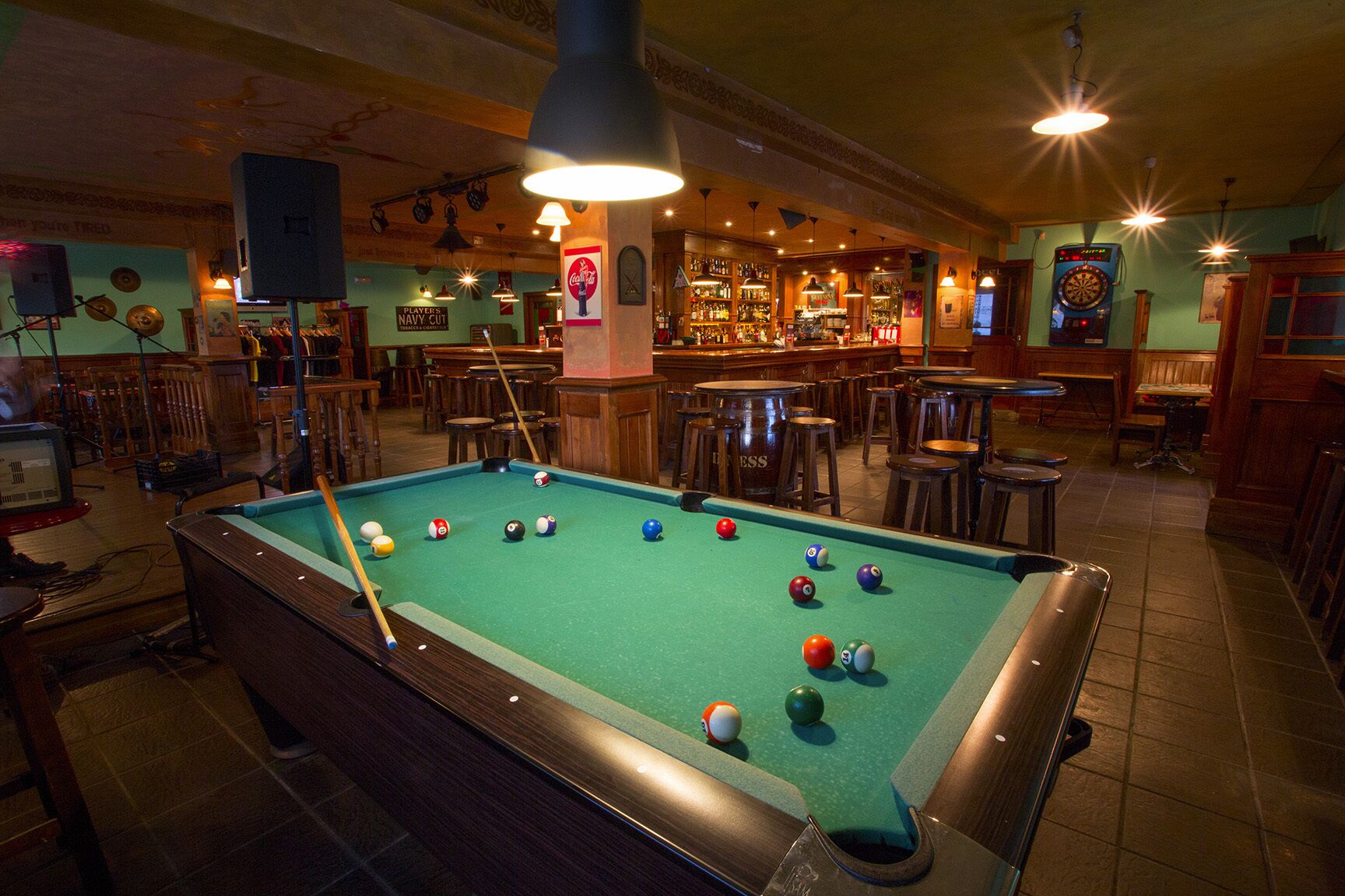 Una mesa de billar en un bar con taburetes y barra.