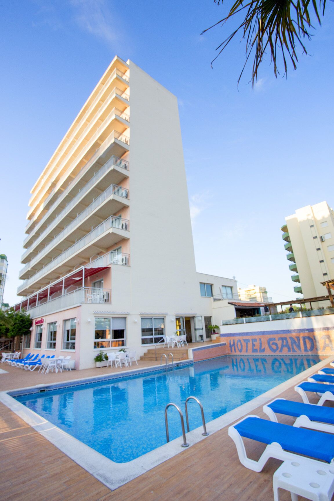 Een hotel met een zwembadgedeelte, inclusief ligbedden en een bord met de tekst 'HOTEL GANDIA HOTEL QUIM'.