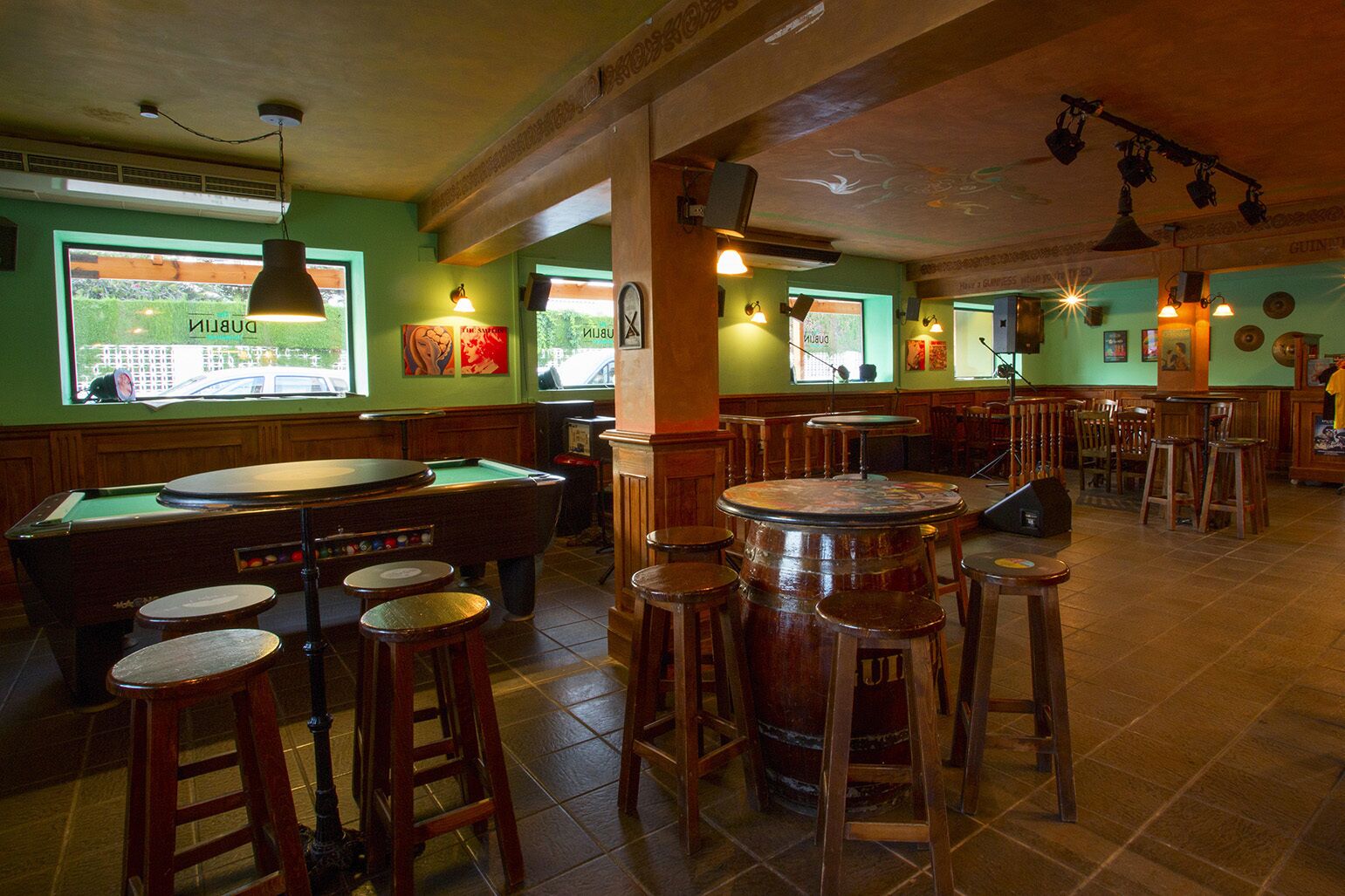 A billiards room with a pool table, stools, and a bar area with stools and a jukebox.