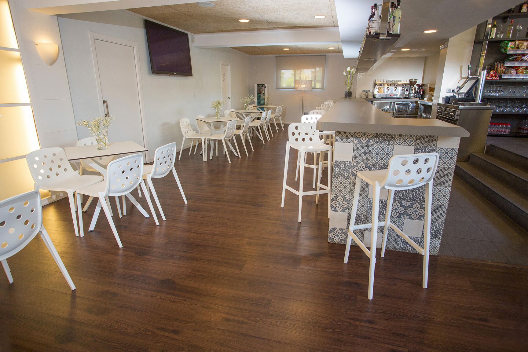 A modern kitchen with a bar area, white chairs, and a wooden floor.
