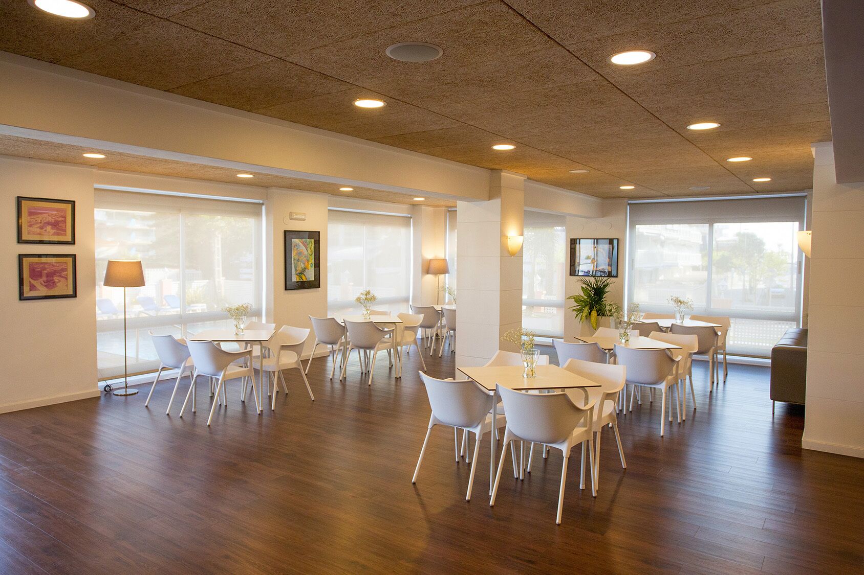 A spacious dining area with multiple tables and chairs, large windows, and ceiling lights.
