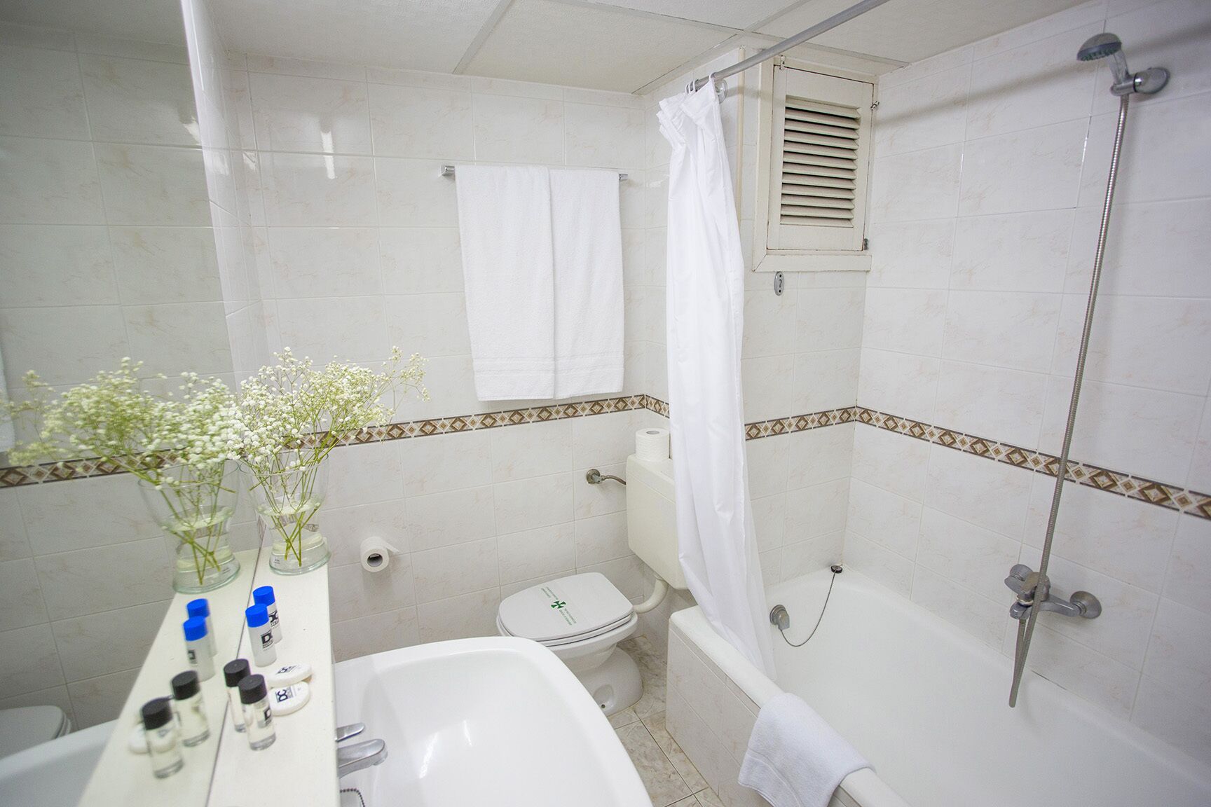 Un baño con bañera, inodoro y lavamanos. Hay artículos de aseo en la encimera.