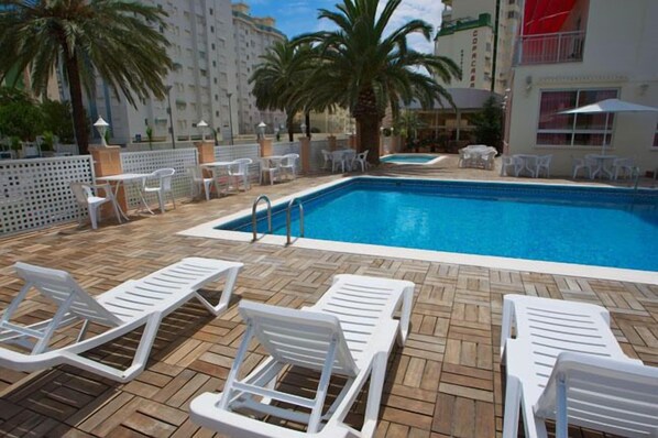 A pool area with white lounge chairs and a wooden deck. - Hotel Gandia (Gandia)