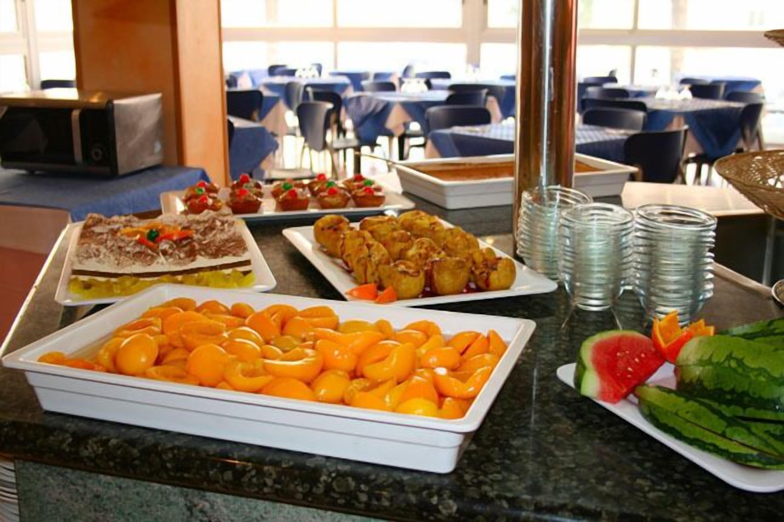 Una mesa de buffet con varios platos, incluyendo una bandeja de rodajas de naranja, un plato de pasteles y una porción de sandía.
