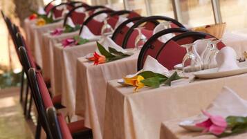 A row of tables with white tablecloths, red chairs, and floral centerpieces.