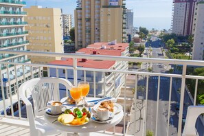 A balcony with a table set for breakfast, including fruit, pastries, and coffee, overlooking a cityscape with tall buildings and a clear sky. - Hotel Gandia (Gandia)