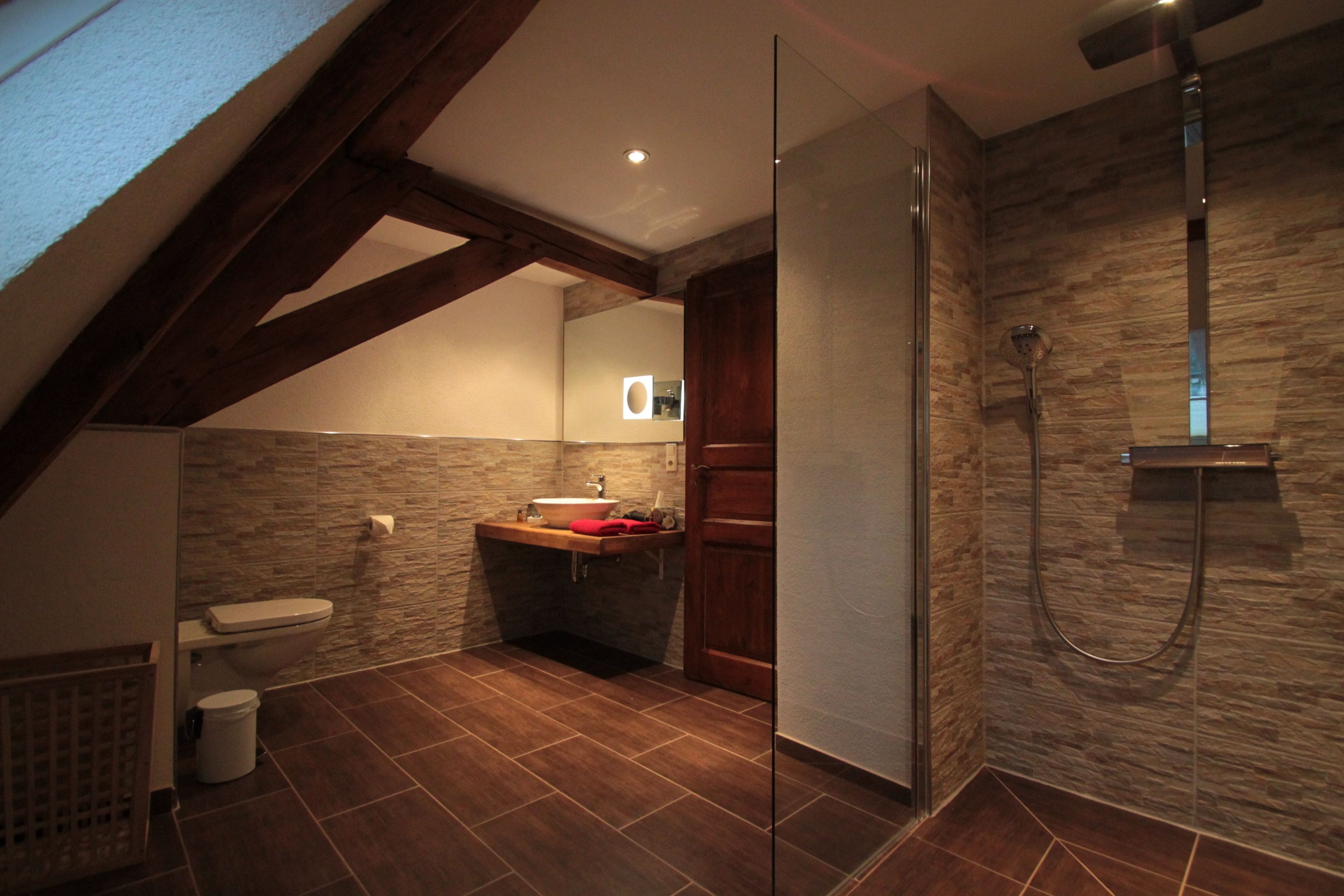 A bathroom with a stone wall, a wooden ceiling, a sink, a toilet, and a shower.