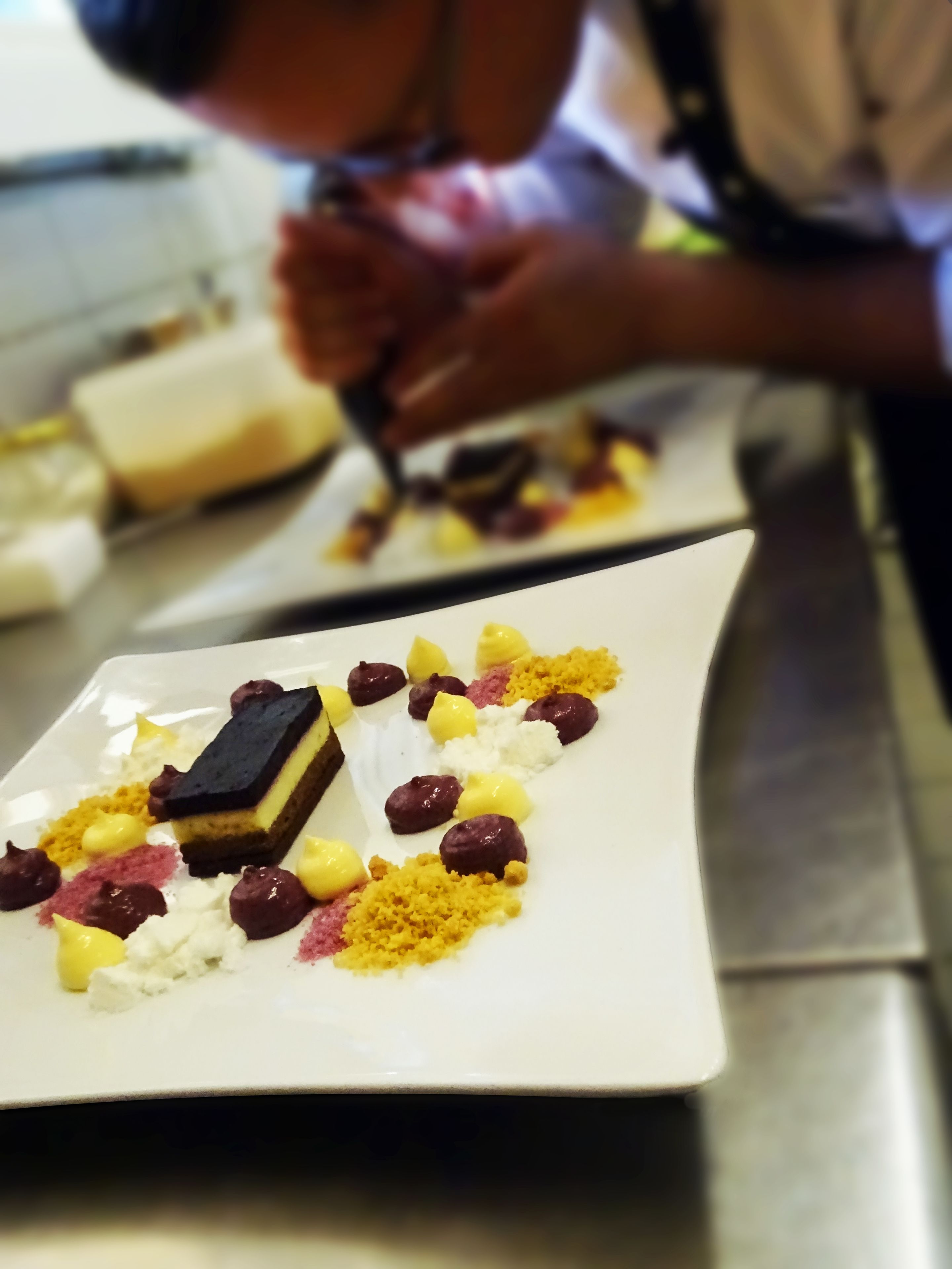 A chef preparing a dessert on a white plate with various toppings.