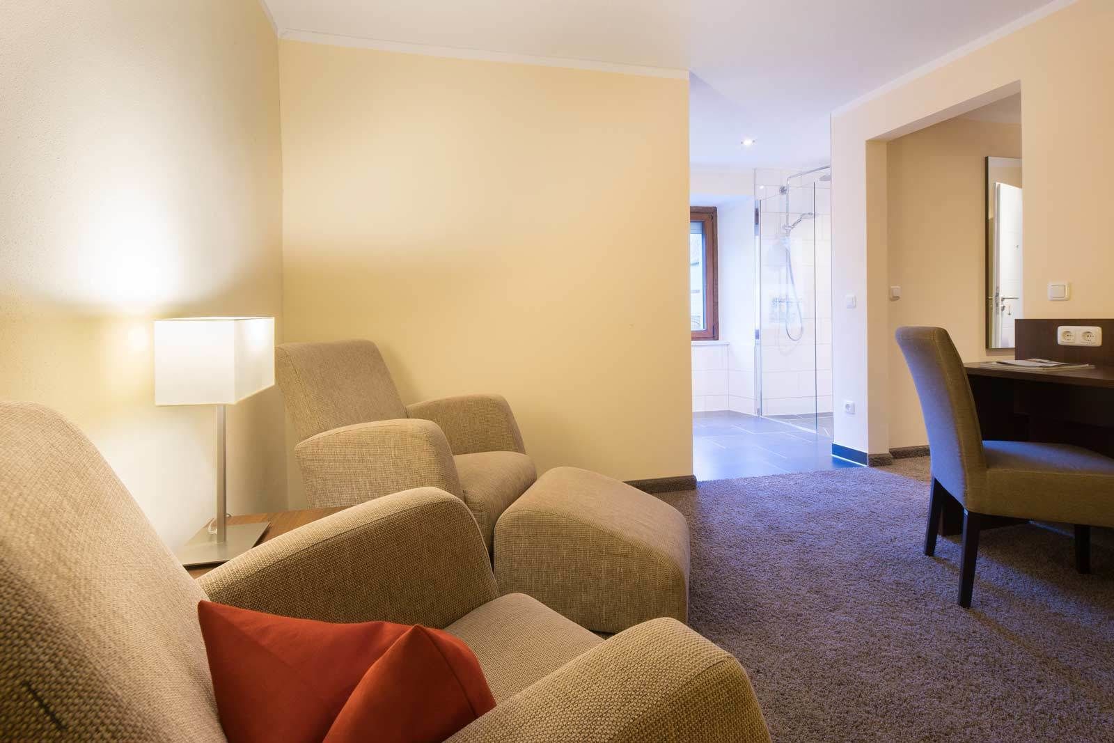 Ein Hotelzimmer mit einer Sofagarnitur, einem Schreibtisch und einer Duschkabine aus Glas.