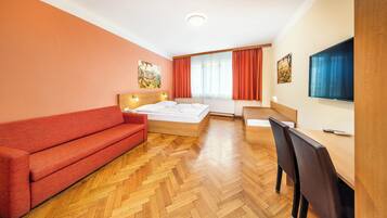 A hotel room with a bed, a red sofa, a wooden desk, and a TV.