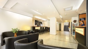 Un vestíbulo moderno de hotel con asientos de cuero negro, una recepción y una escalera que conduce a los pisos superiores.