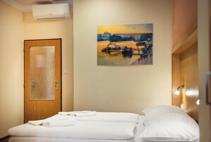 Quarto de hotel com cama, porta de madeira, pintura de um pôr do sol e ar condicionado fixado na parede.