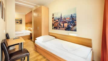 Ein kleines Hotelzimmer mit einem Einzelbett, einem Schreibtisch mit Stuhl, einem Holzschrank und einem Stadtbild an der Wand.