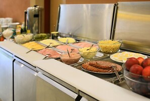 Buffet com diversas opções de comida, incluindo frutas, queijos e carnes.