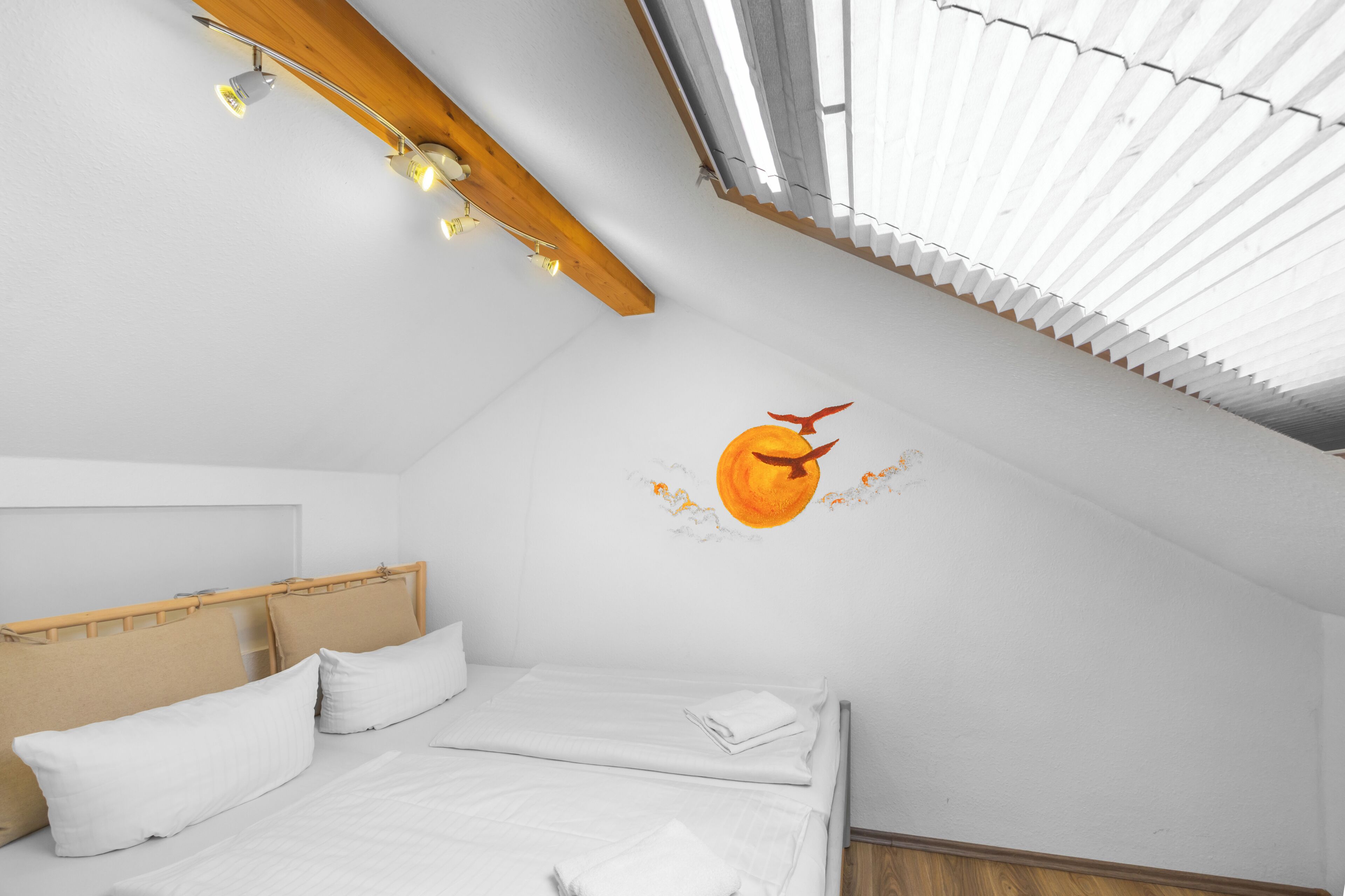 Ein Schlafzimmer mit Bett, Holz-Kopfteil, weißer Bettwäsche, Wandgemälde und einem Dachfenster.