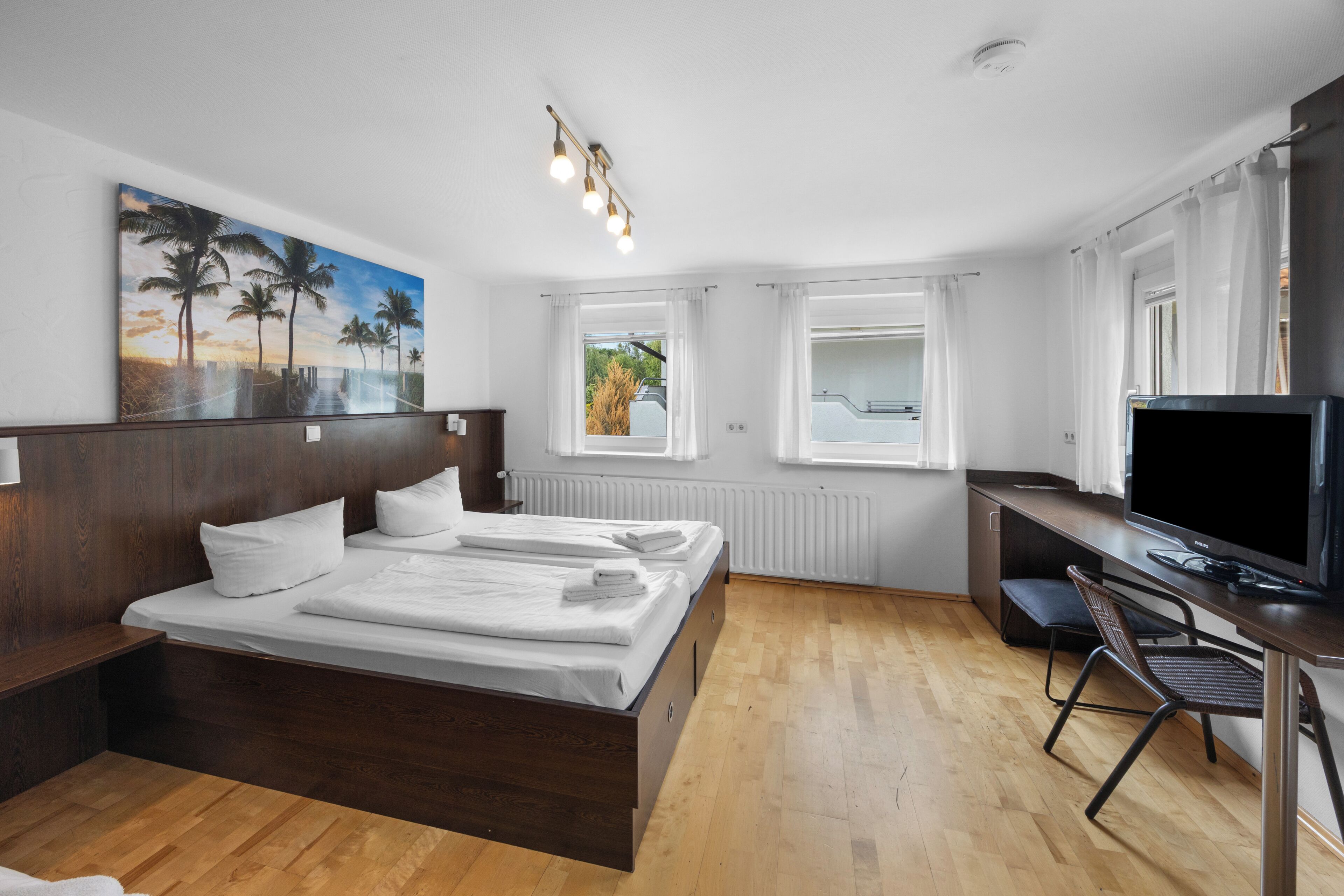 A hotel room with a bed, a desk with a TV, a chair, a window with curtains, and a painting on the wall.