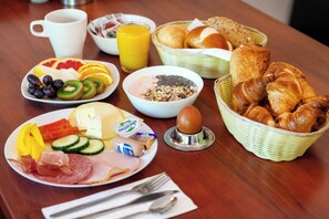 A breakfast setting with plates of food, a basket of croissants, a coffee cup, and a juice glass.