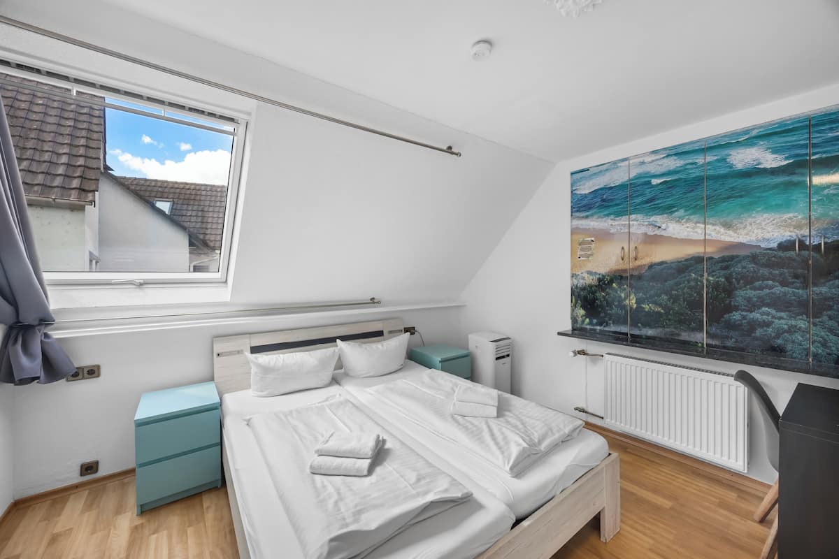 A bedroom with a bed, a window, a radiator, and a wall-mounted artwork.