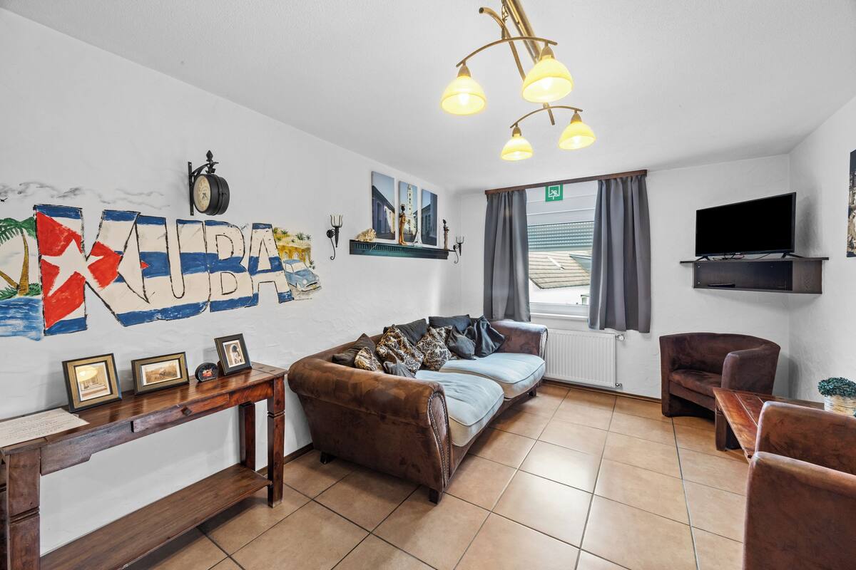 A furnished living room with a sofa, armchairs, a TV, a wall clock, and artwork.