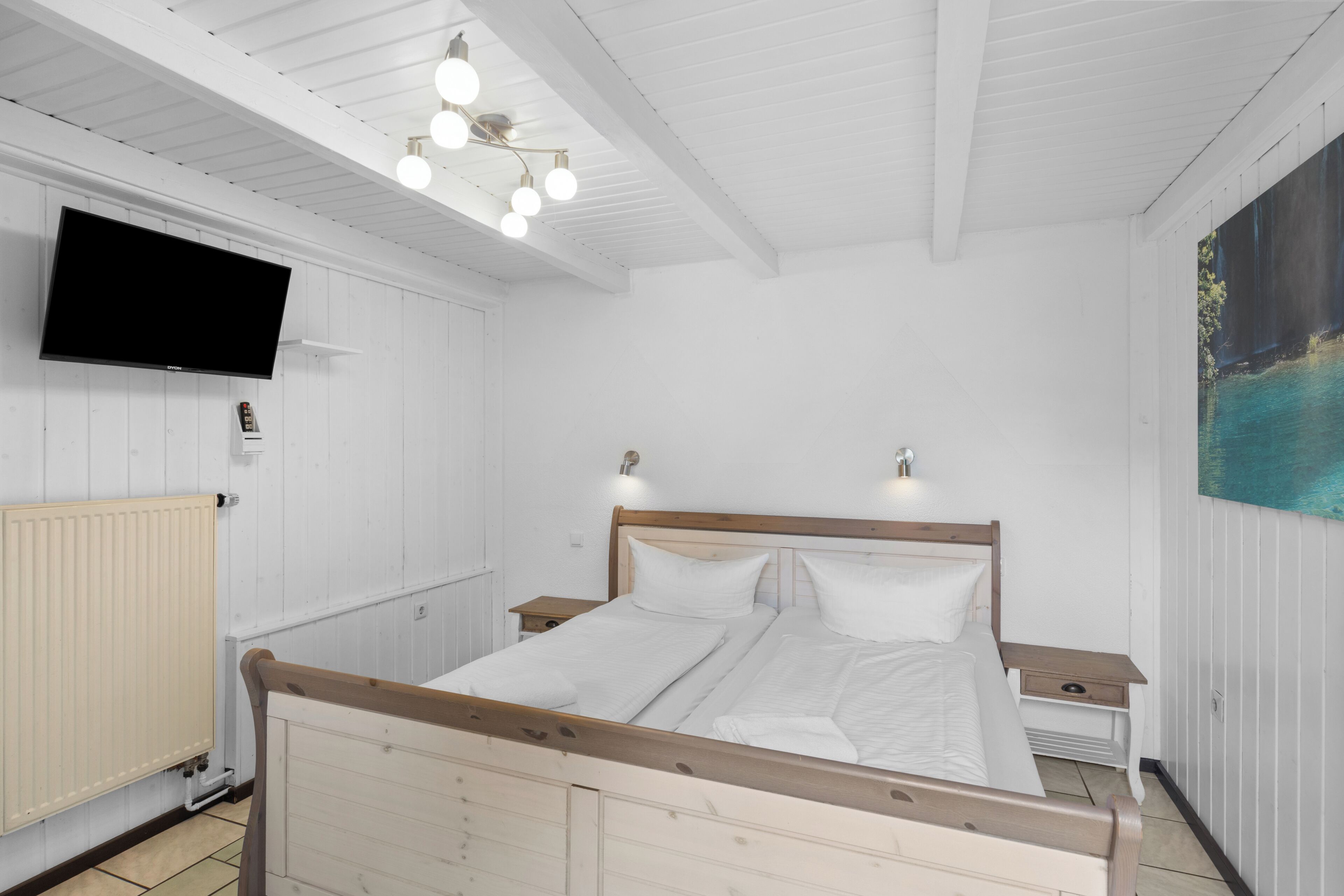 Ein Schlafzimmer mit einem hölzernen Bett, Nachttischen, einem Wand-Fernseher und einem Gemälde an der Wand.