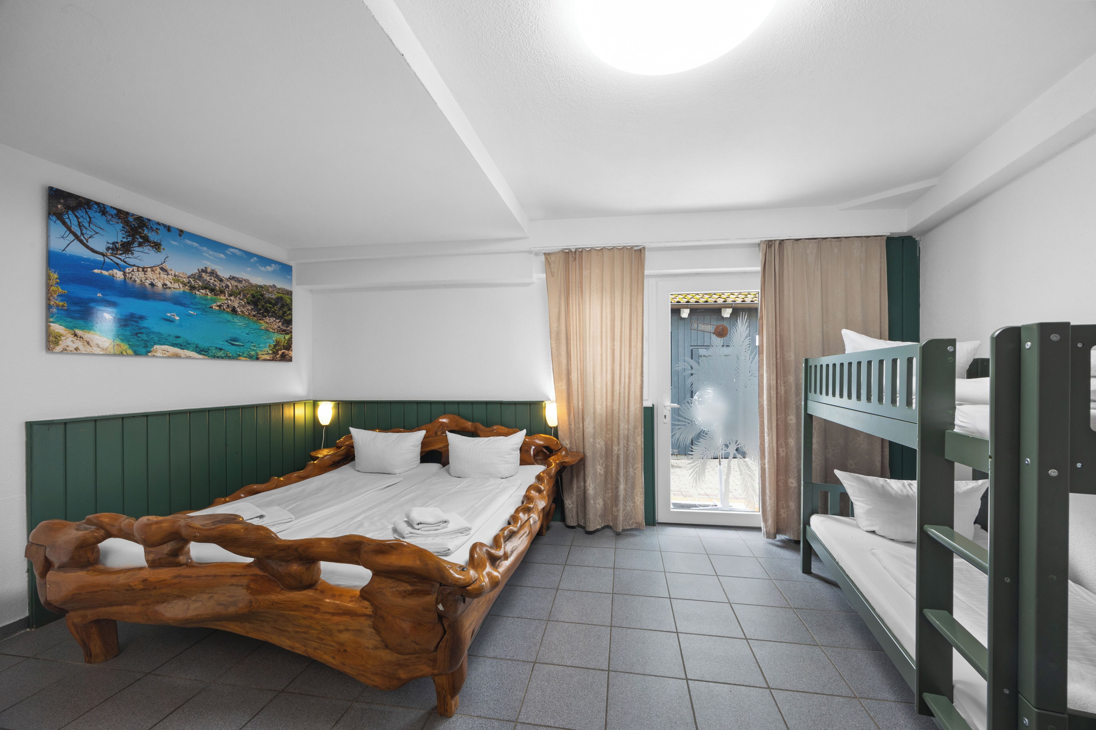 Una habitación con una cama de madera, una cama litera, un cuadro de una escena costera y vistas a través de una puerta.