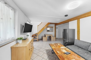 A modern living room with a wooden staircase, a flat-screen TV, a sofa, and a dining table. - Gaestehaus Parkblick (Rust)