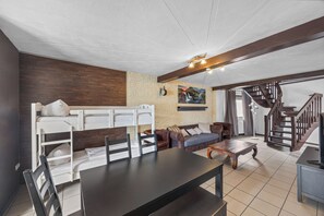 Une pièce avec des lits superposés, un canapé, une table à manger et un escalier.