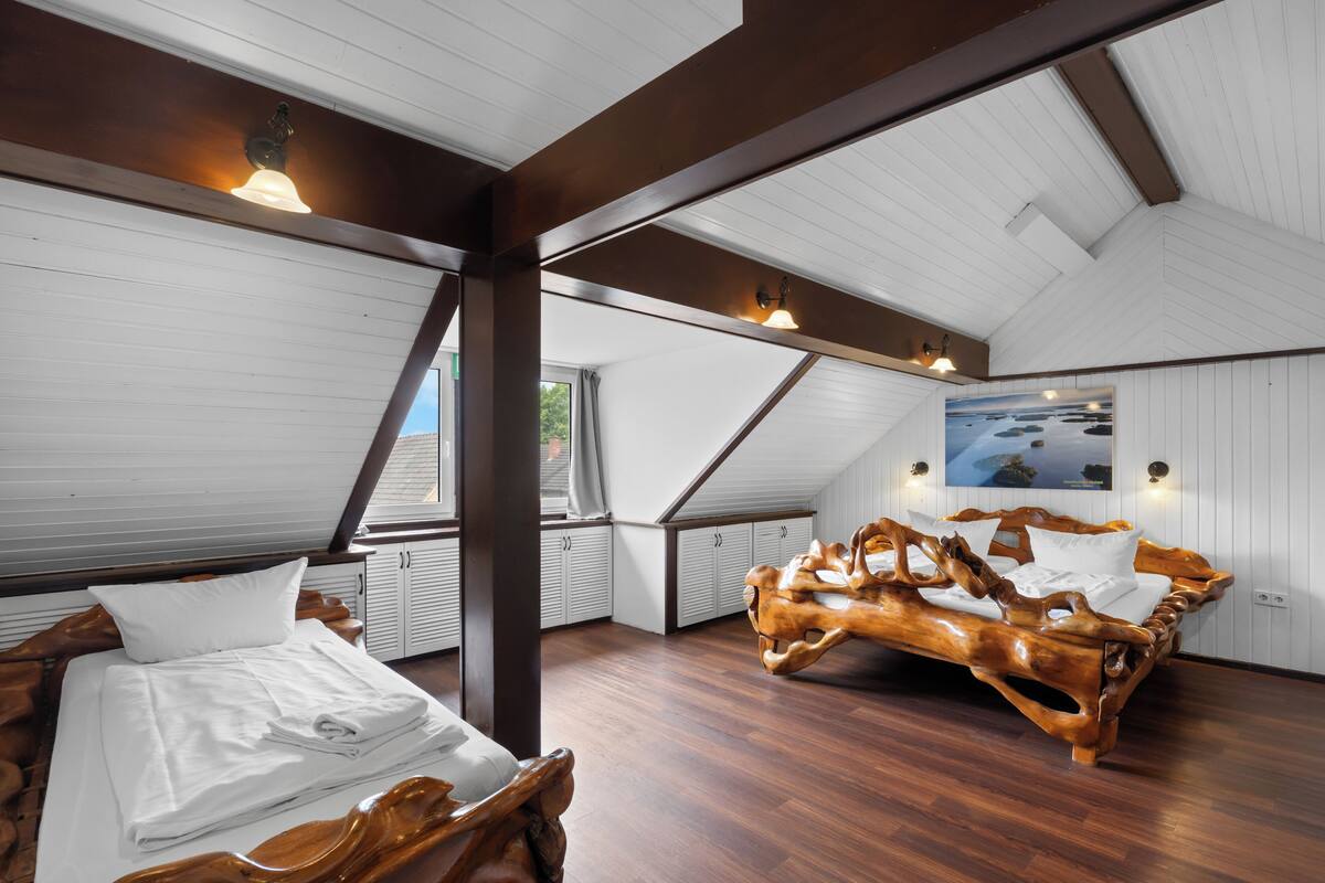 A room with a sloped ceiling, a wooden bed, a window, and a painting on the wall.