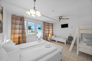 Une chambre d’hôtel avec un lit, un bureau, une chaise, une télévision, un lit superposé et une vue sur des palmiers.