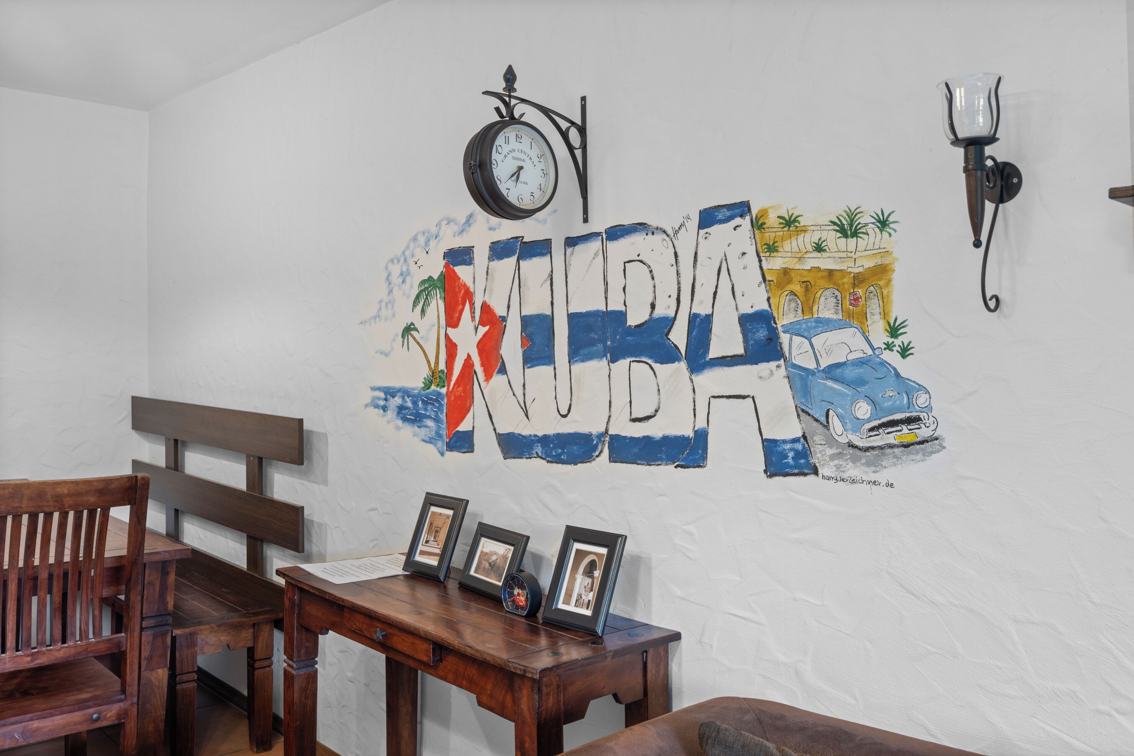 Parede com um mural pintado retratando um carro e palmeiras, um relógio e um aplique.