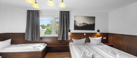 Ein Hotelzimmer mit zwei Betten, einem großen Fenster mit Vorhängen, einem Stadtbildgemälde und einer Deckenleuchte.