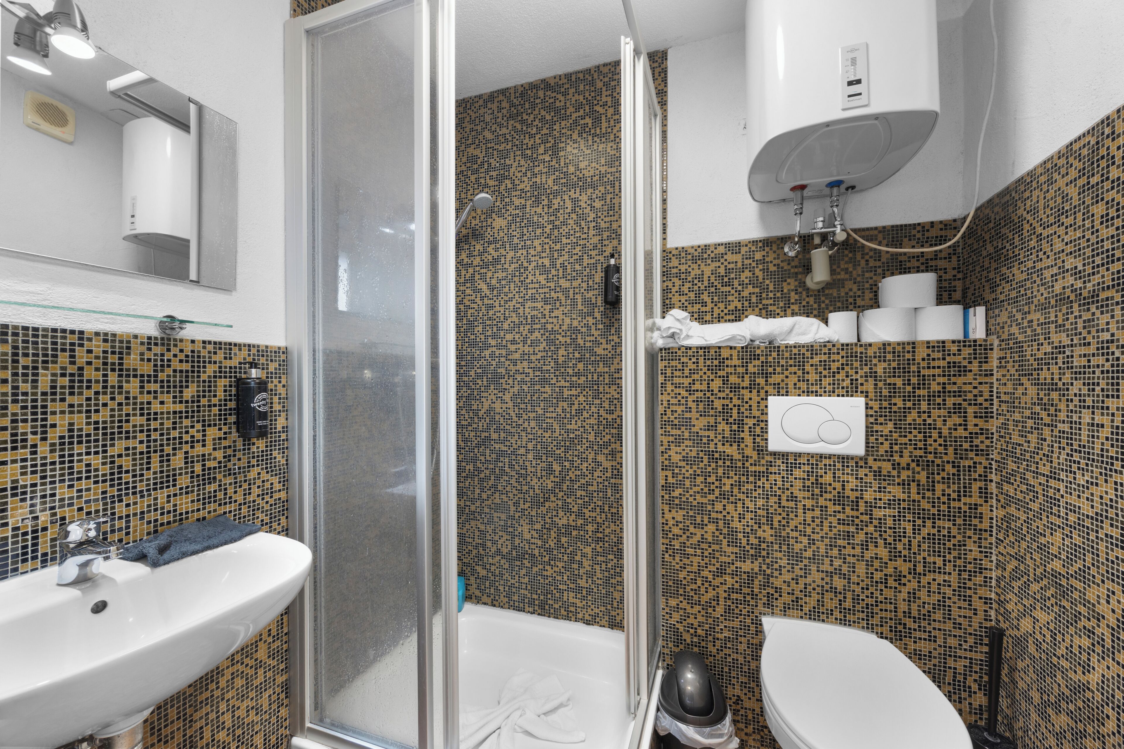 A bathroom with a shower, toilet, sink, and tiled walls.