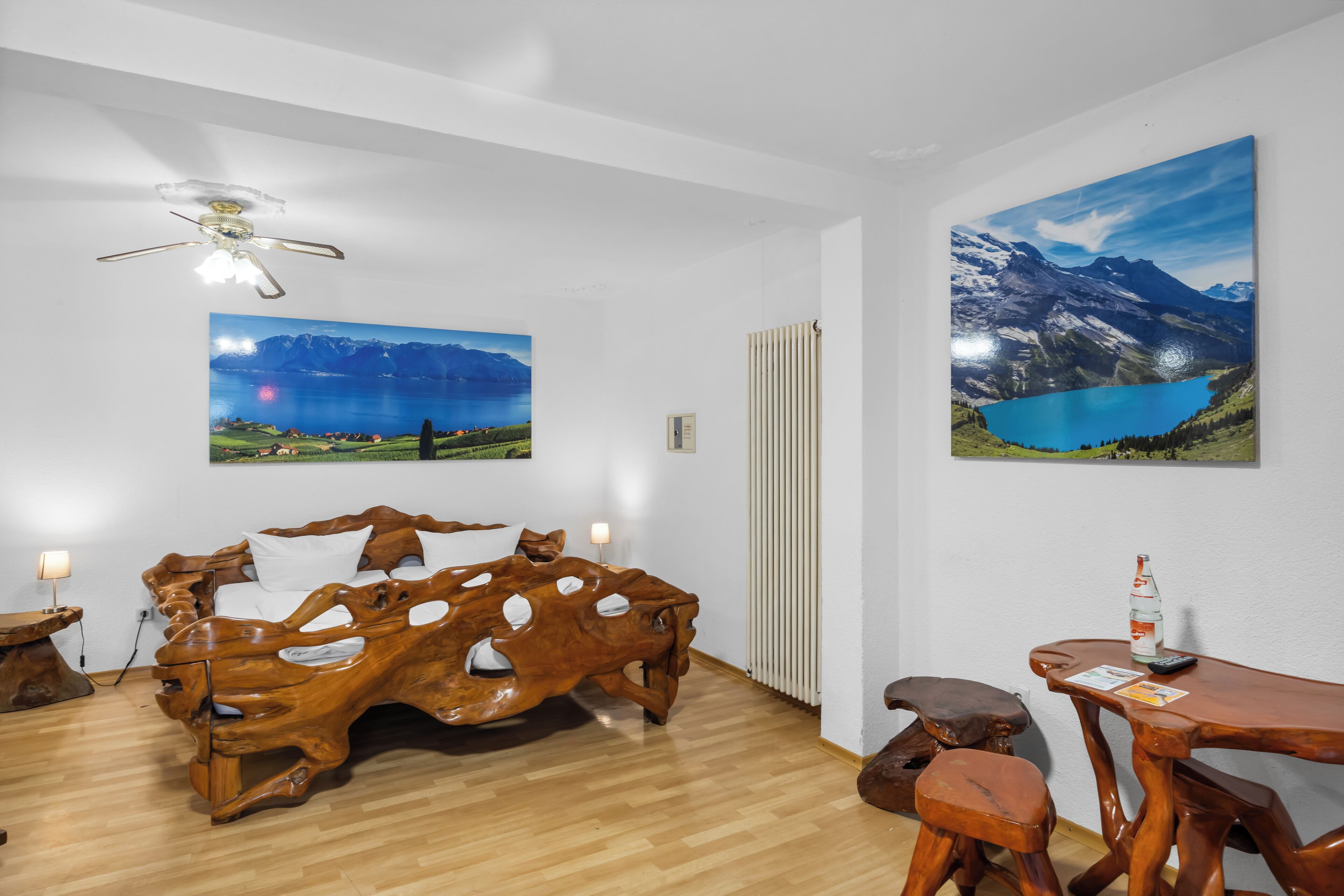 Una habitación con una cama de madera singular, muebles de madera y dos grandes cuadros con paisajes en las paredes.