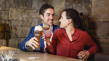 Ein Mann und eine Frau sitzen an einer Bar mit Steinwänden und halten Biergläser in der Hand.