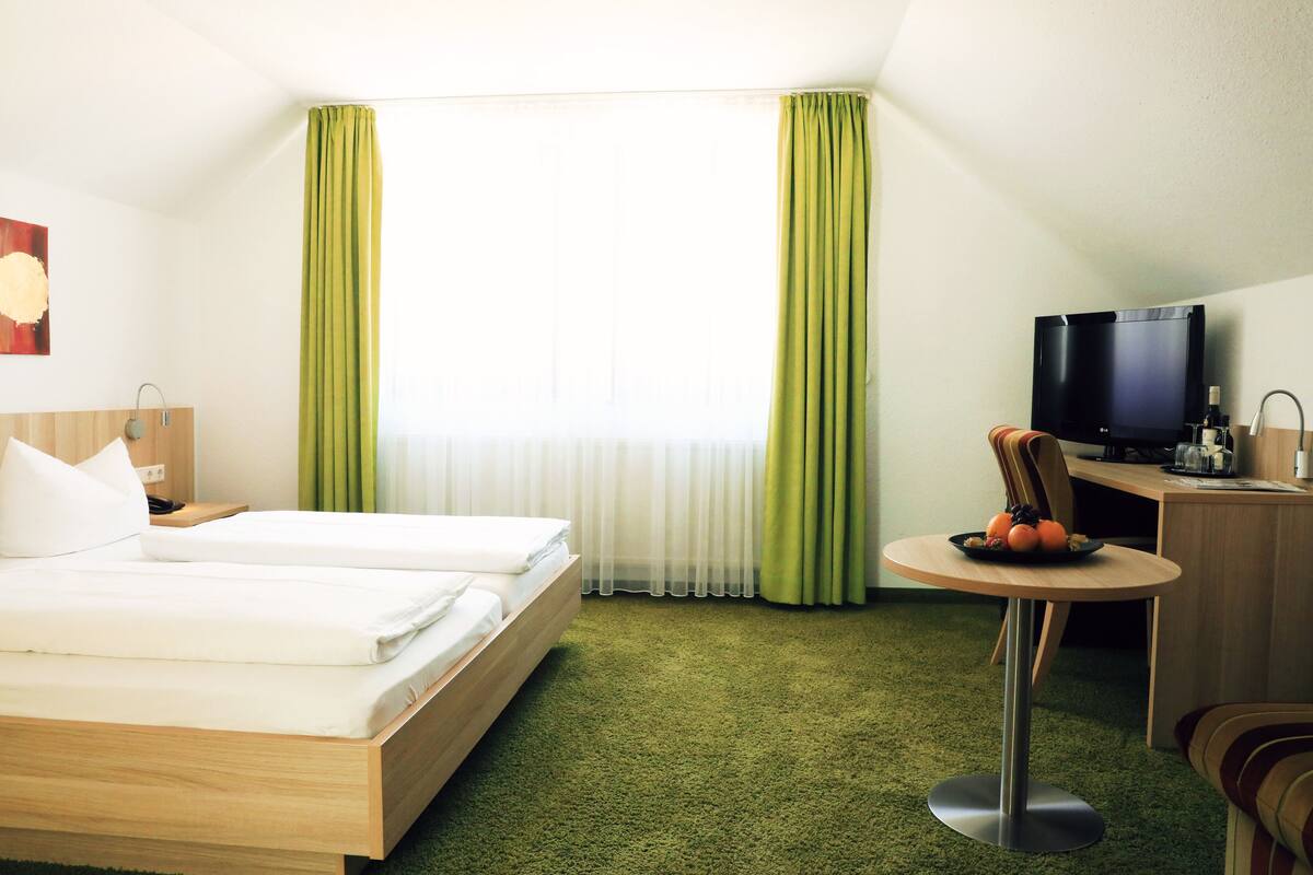 A hotel room with a bed, a desk with a television, and a small table with fruit.