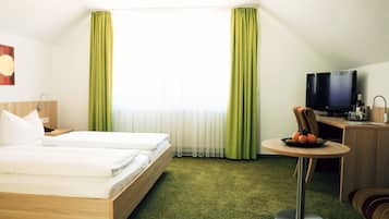 A hotel room with a bed, a desk with a television, and a small table with fruit.