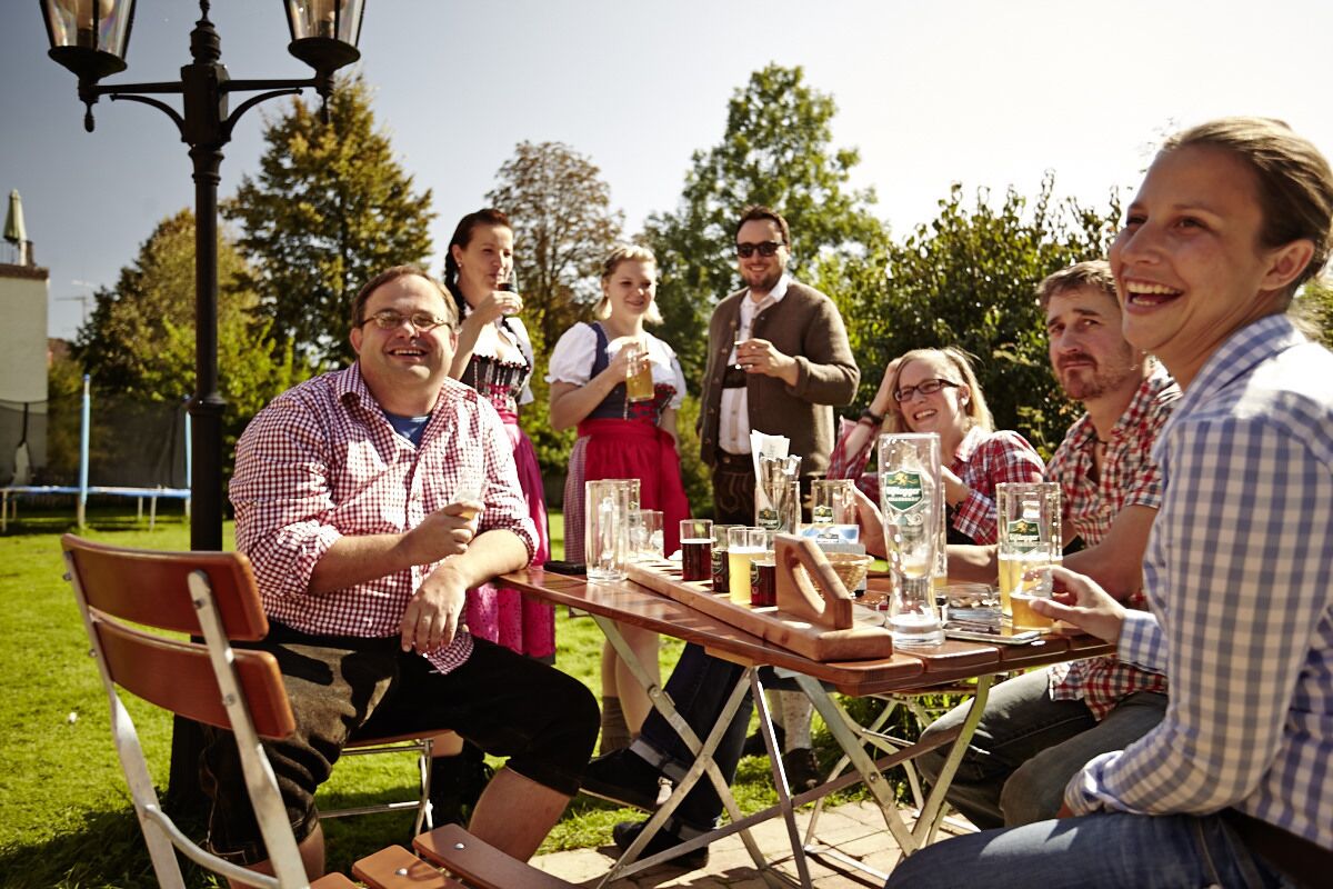Eine Gruppe von Personen sitzt an einem Tisch im Freien, umgeben von Pflanzen und einer Lampe.