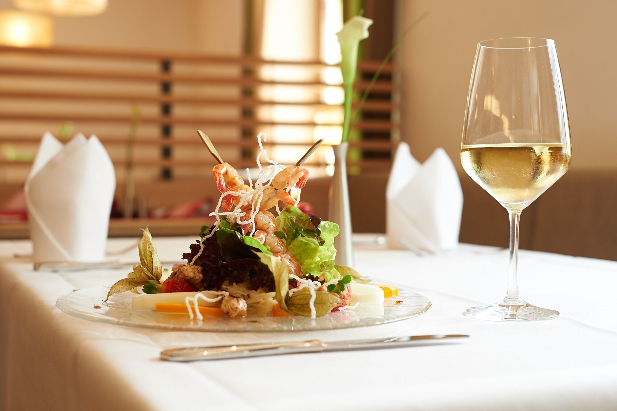 A table with a glass of white wine and a plate of food.