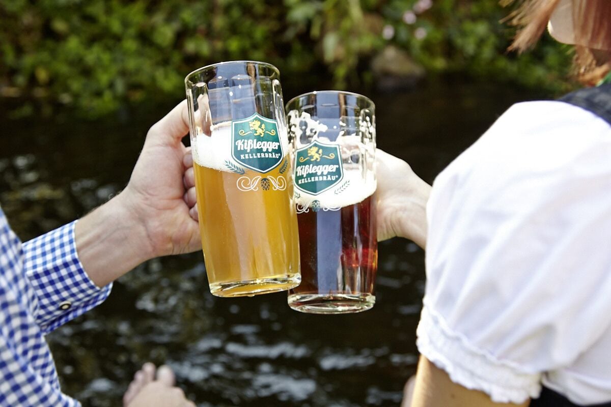 Dos personas sosteniendo vasos de cerveza con el logotipo de la marca 'Kiflegger Kellerbrau'.