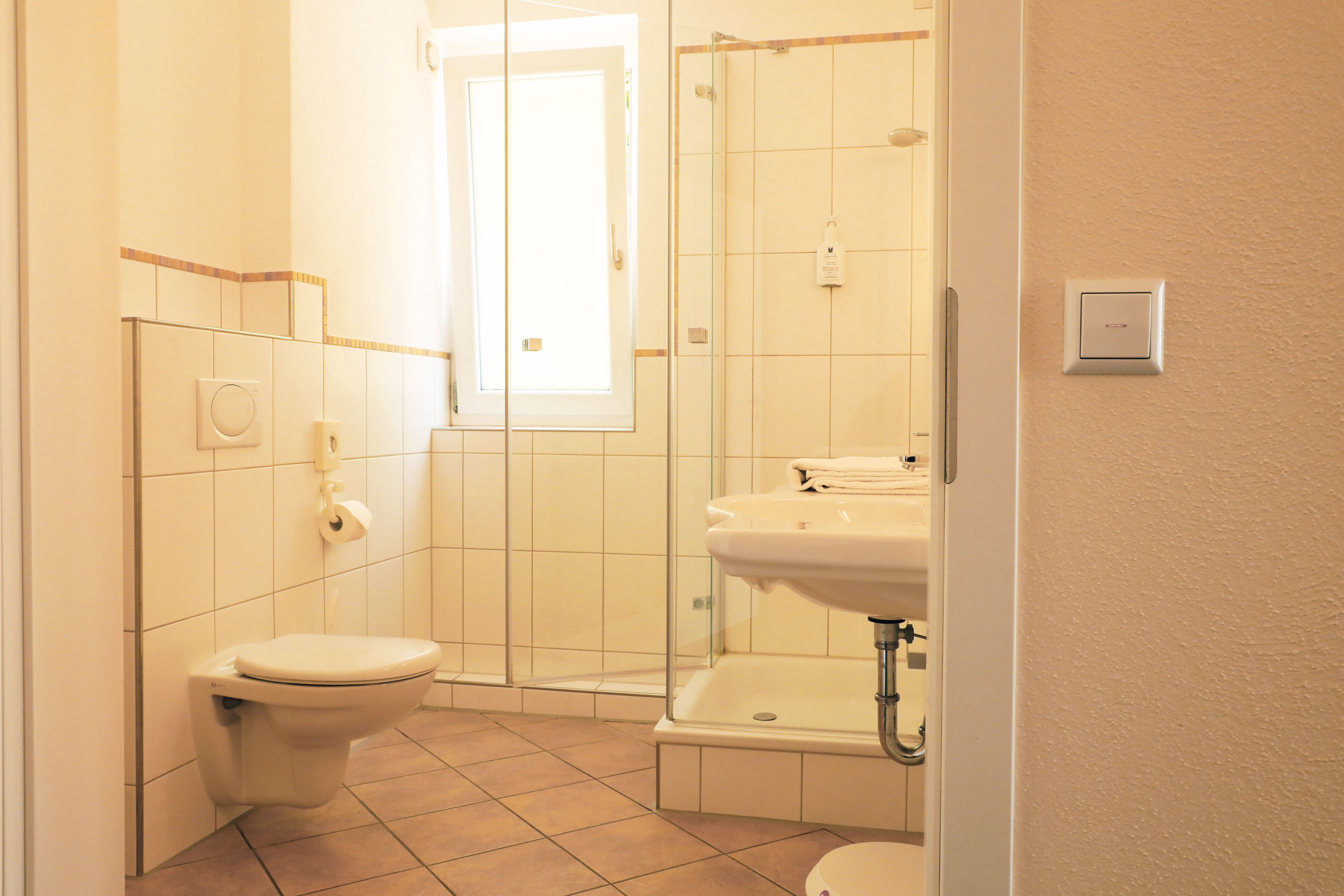 Een kleine, goed verlichte badkamer met toilet, wastafel en douche.