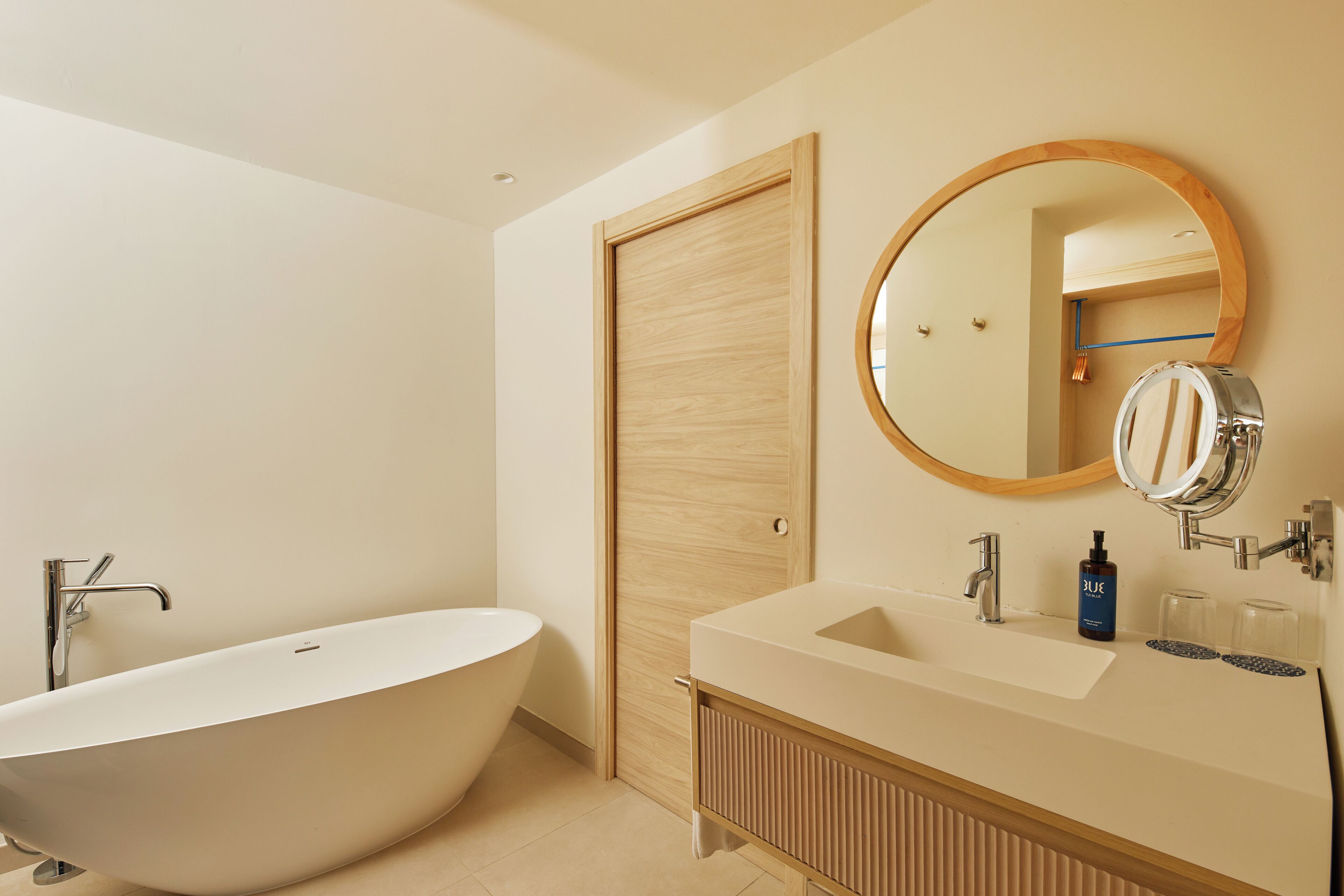 A modern bathroom with a freestanding bathtub, a vanity with a mirror, and a wooden door.